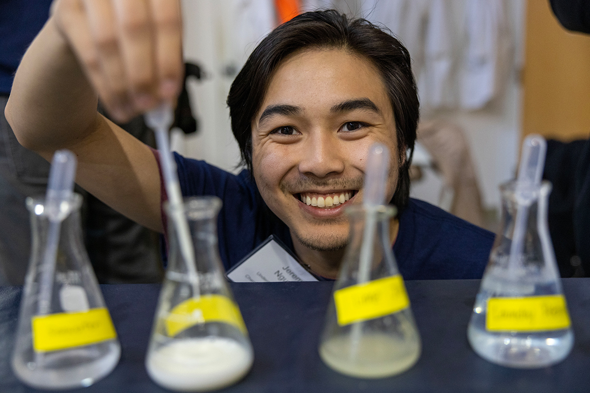 student smiling in front of four beakers holding a pipette