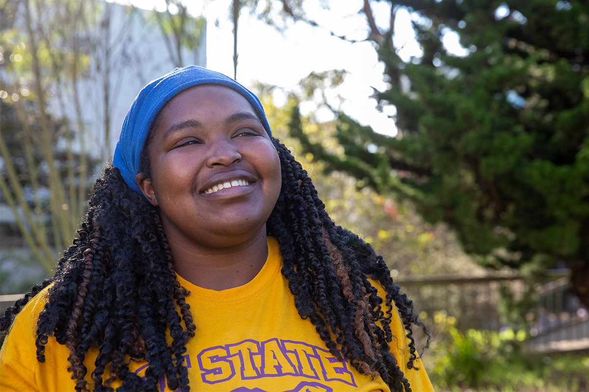 student smiling to the sky with a yellow SF State shirt and blue headband 