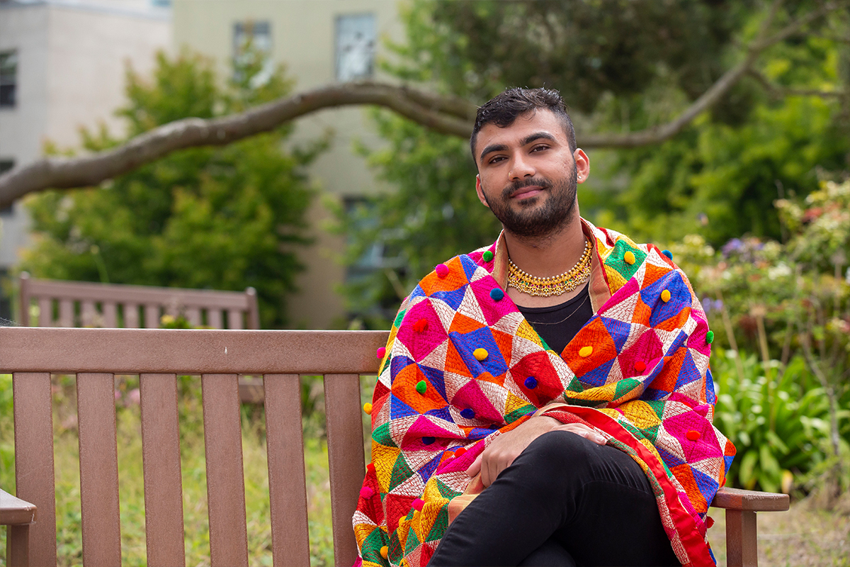 student wearing colorful garment and jewelry sitting on a wooden bench